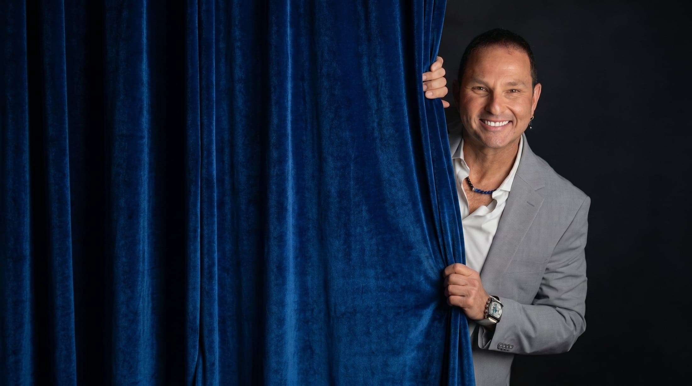 Guy Bavli peeking from behind a blue velvet curtain