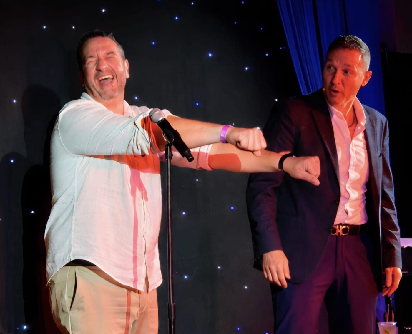 An audience volunteer laughing on stage beside Guy Bavli